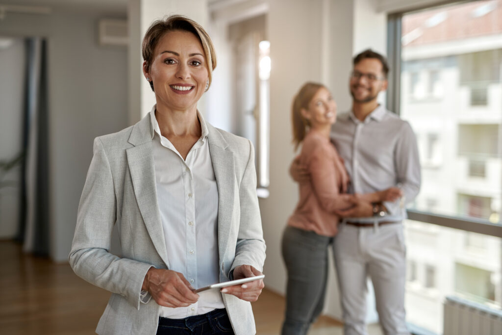Portrait of happy real estate agent with a couple in the backgro